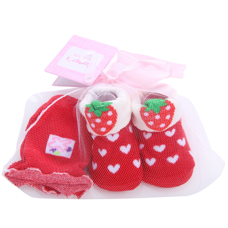 Red baby booties with strawberry details and white heart patterns, paired with matching socks. Packaged in a sheer mesh bag with a pink ribbon and tag.