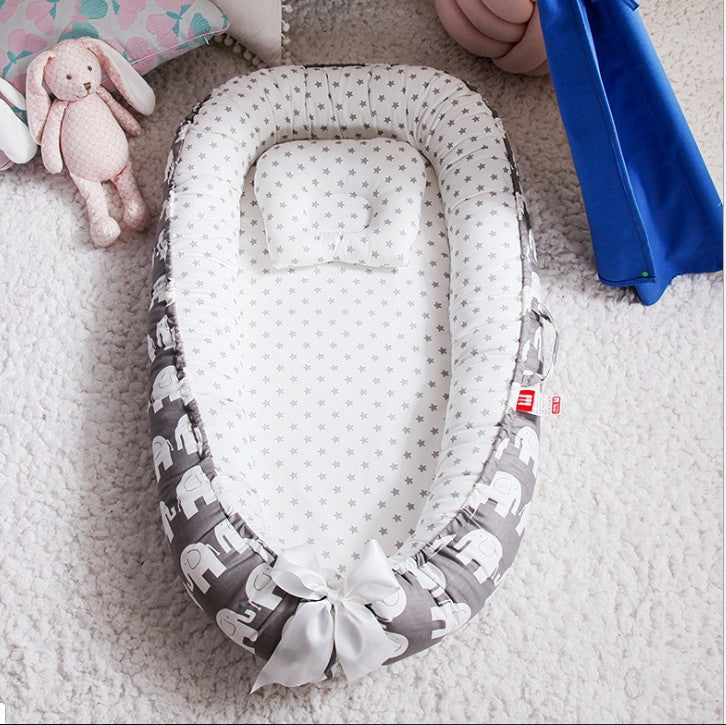 A cozy baby nest with a star-patterned interior and elephant design on the sides, featuring a small pillow, placed on a soft, white carpet next to a plush pink bunny toy.