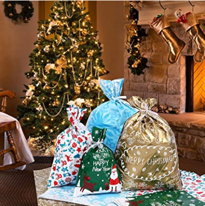 Christmas scene with a decorated tree, stockings on a fireplace, and festive gift bags labeled "Merry Christmas" and "Happy New Year" in front, surrounded by lit garlands.
