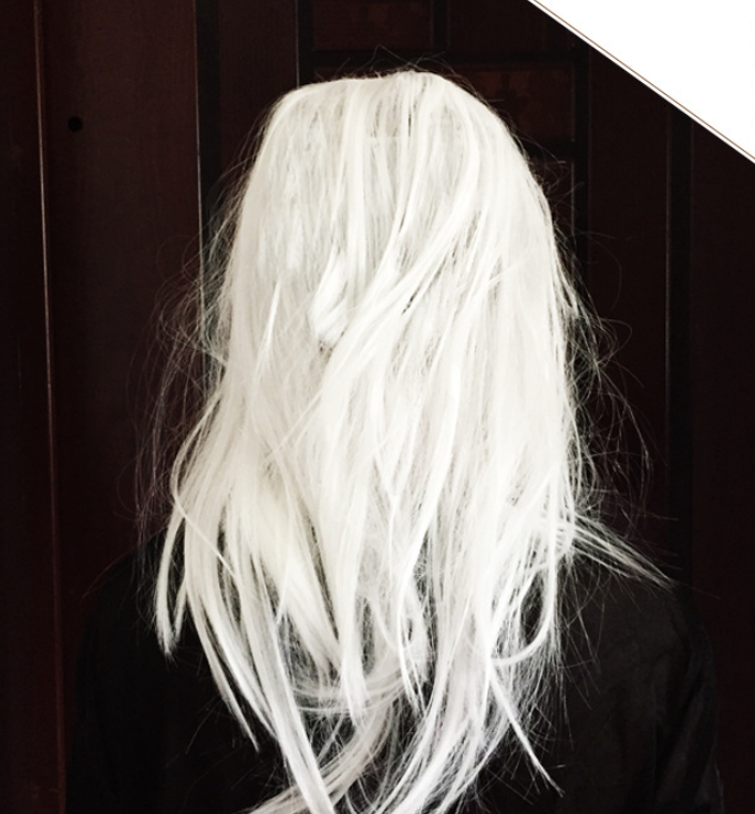Back view of a person with long, tousled white hair against a dark background, wearing a black top.
