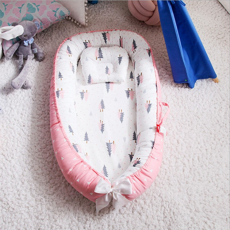 Baby nest with a pink bow and forest print, placed on a soft, textured carpet. Nearby are plush toys and a blue play tent, creating a cozy, playful environment.