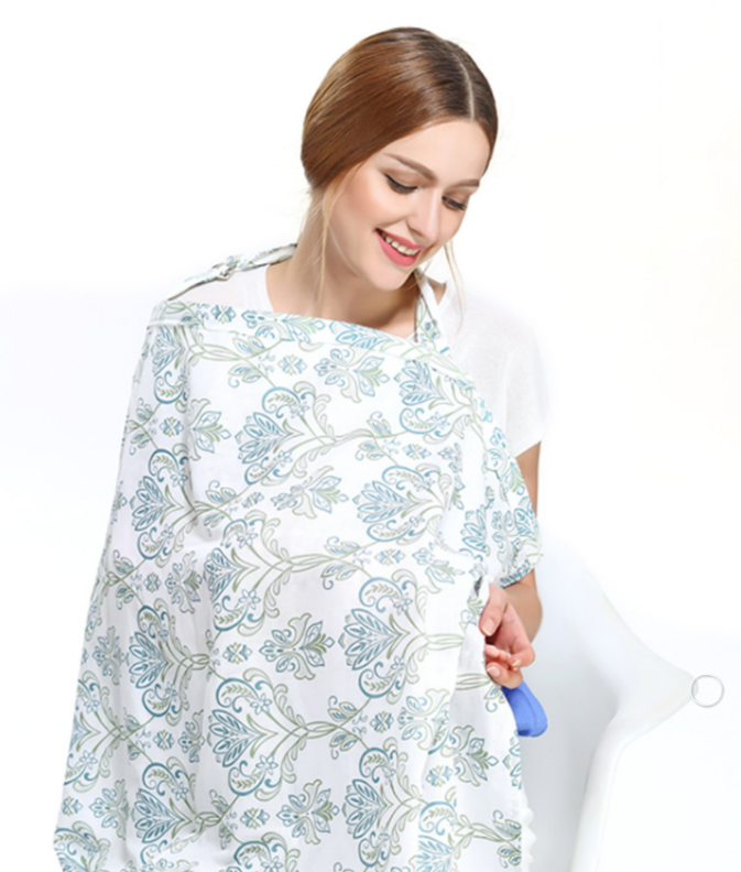 Smiling woman sitting and using a floral patterned nursing cover, holding a baby. The cover is white with blue and green designs, creating a calm and soothing scene.