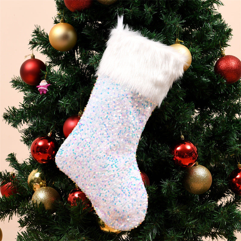 A white faux fur Christmas stocking hangs on a tree decorated with red and gold ornaments. The stocking is adorned with iridescent sequins, adding a shimmering effect.
