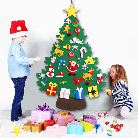 Two children decorate a felt Christmas tree on the wall with colorful ornaments and gifts at the base. One child wears a Santa hat. The scene is festive and cheerful.
