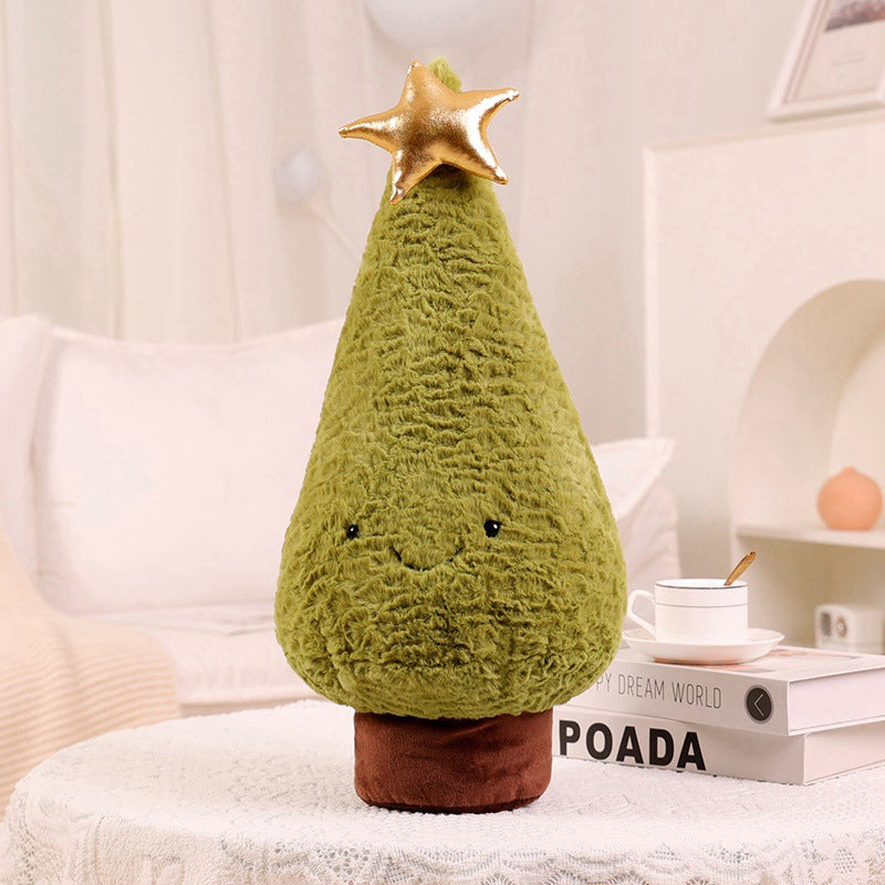 Cute plush toy shaped like a Christmas tree with a golden star on top is placed on a table. It features a small face and is set against a cozy living room background.