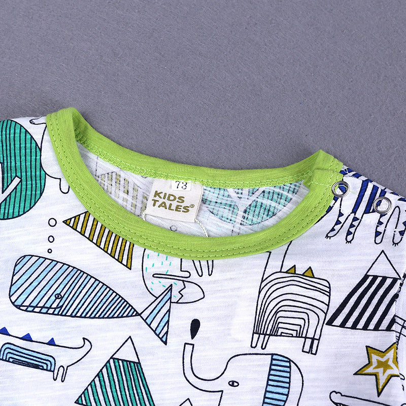 Close-up of a baby shirt with a green-trimmed neckline. The fabric features playful animal and geometric prints in blue and green tones. A Kids Tales label is visible.