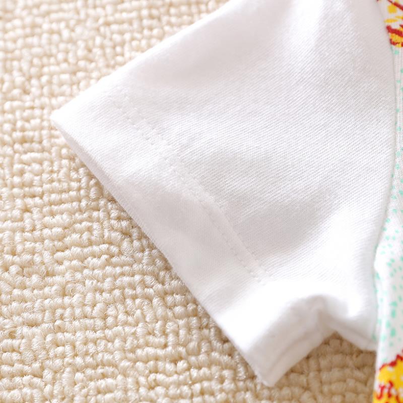 Close-up of a white short sleeve T-shirt on a textured beige carpet. The fabric has a smooth finish, and part of a colorful pattern is visible at the seam.