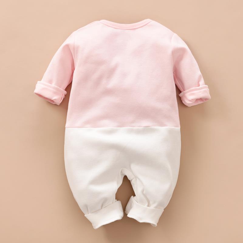 Pink and white baby romper with long sleeves and rolled cuffs, displayed on a beige background. The top half is pink, and the bottom half is white, with a soft, casual style.