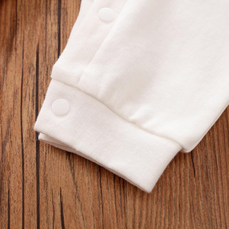 White baby onesie sleeve on a wooden surface, featuring a folded cuff with snap button closures for easy dressing. The wood grain adds texture and a warm contrast.