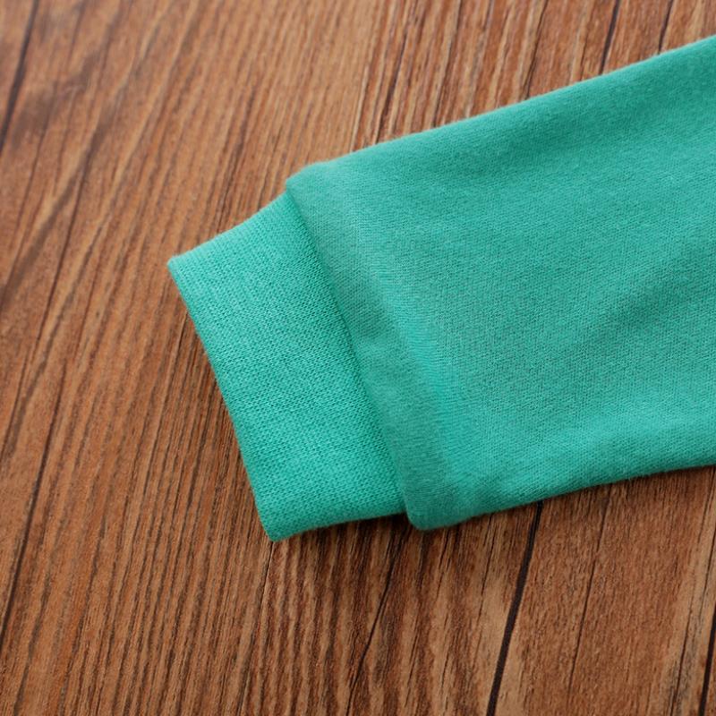 Close-up of a turquoise fabric sleeve cuff on a wooden surface, showing the texture and stitching details.