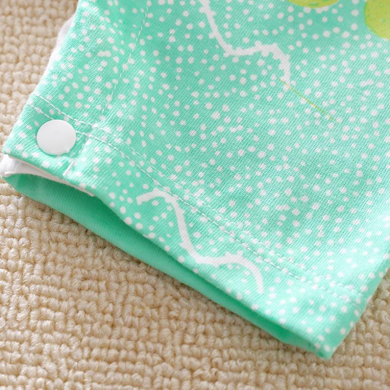 Close-up of a mint green fabric with white polka dots and abstract lines, featuring a white snap button on textured beige carpet.
