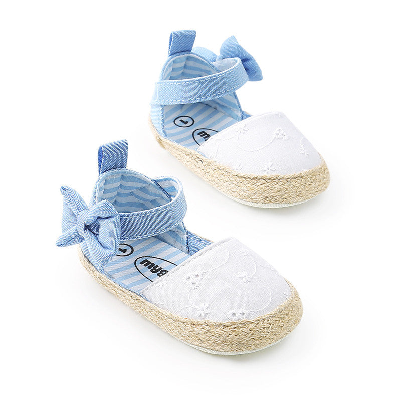 Light blue baby shoes with ankle straps, bows, and white embroidered floral fronts on woven straw soles. The interior has a blue and white striped pattern.