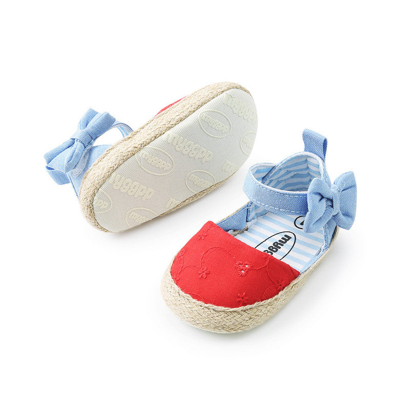 Red canvas baby shoes with woven soles and light blue ankle straps featuring bows. The inner lining is blue and white striped, and the soles have embossed branding.