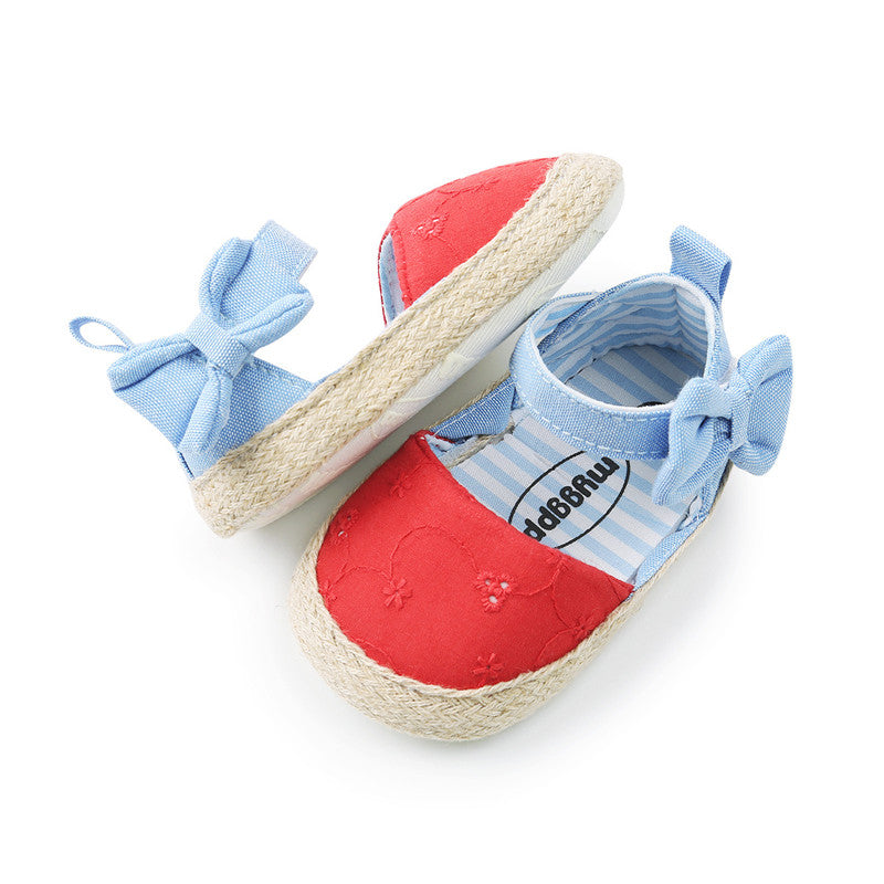 Baby sandals with red fabric tops, blue ankle straps with bows, and straw-textured soles. The interior features a blue and white striped pattern.