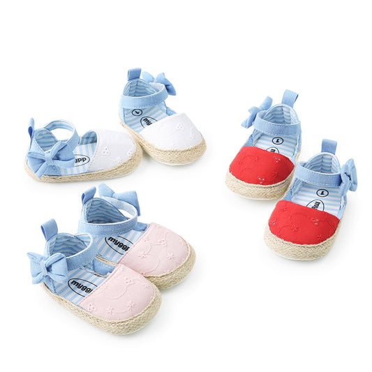 Three pairs of baby shoes with blue straps and bows: one pair is white, another pink, and the third red. The shoes have a woven sole.