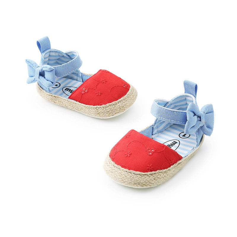Red baby shoes with blue straps and bows, featuring a textured floral pattern on the front and a woven-style sole, perfect for infants.