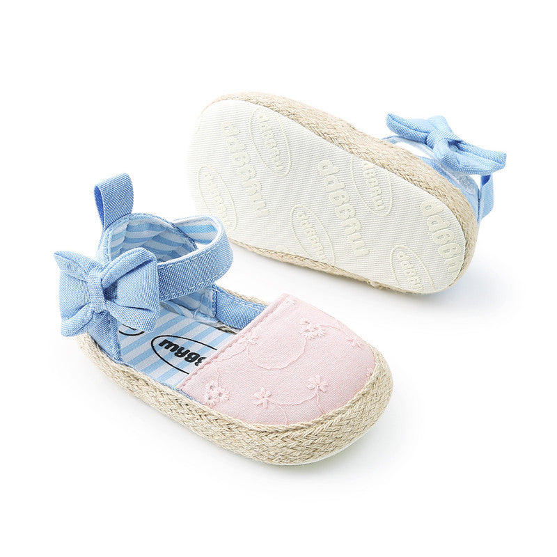 Pink baby shoes with embroidered floral design, blue strap, and bow. One shoe shows the "mygbb" brand on the sole. The interiors are blue and white striped.