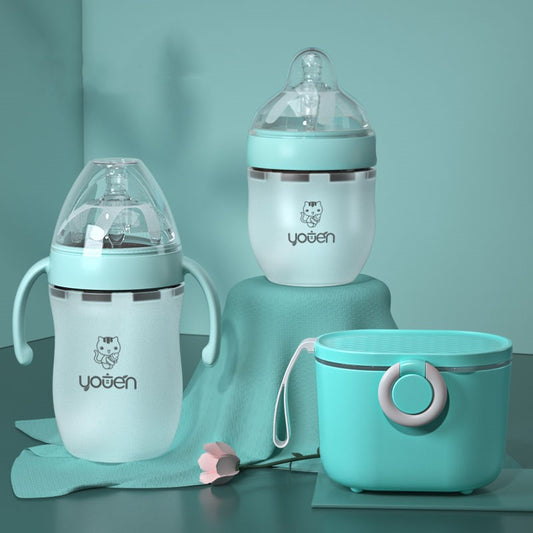 Three pastel-colored baby bottles and a matching container are displayed on a soft blue surface, adorned with a small flower.