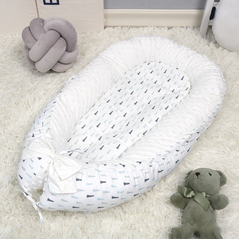 Cozy baby nest with a white and blue tree pattern on a plush rug, accompanied by a soft green teddy bear and a grey knot pillow in a serene nursery setting.