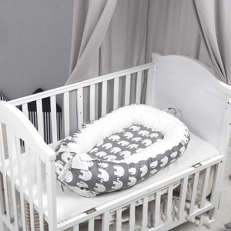 White crib with a gray elephant-patterned baby nest. The crib has a soft mattress, surrounded by light gray drapes and plush cushions with black and white stripes.