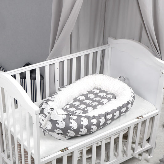 White crib with a gray elephant-patterned baby nest. The crib has a soft mattress, surrounded by light gray drapes and plush cushions with black and white stripes.
