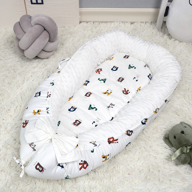 A cozy baby lounger with colorful animal prints on a white fluffy rug, accompanied by a grey knot pillow and a stuffed green teddy bear.