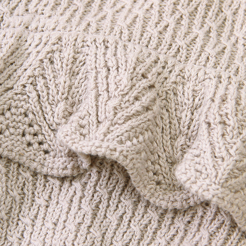 Close-up of beige knitted fabric with a textured, zigzag pattern and ruffled edges, showcasing intricate detailing and soft material.