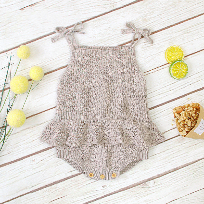 Knitted beige baby romper with ruffled waist and shoulder ties, set on a wooden background. Decorated with yellow spheres, lemon slices, and a small pouch of popcorn.