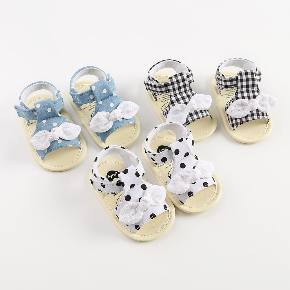 Three pairs of baby sandals on a white background: blue with white polka dots, black and white gingham, and white with black polka dots. Each pair features a fabric bow.