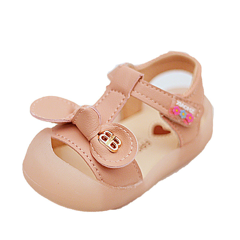 Peach-colored toddler sandal with a heart cutout, ankle strap, and decorative gold buckle. Features pink and blue flower accents on the side.