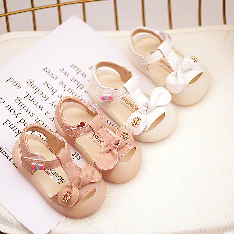 Four pairs of toddler shoes with bows, in pink and white, displayed on a white surface with printed text. The shoes have gold embellishments and floral details.