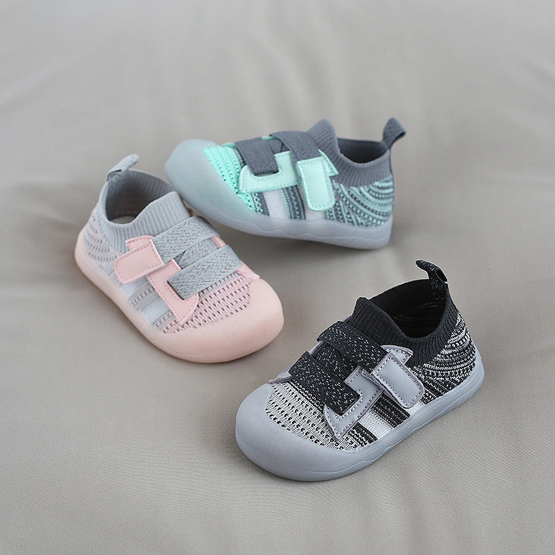 Three toddler shoes are arranged on a neutral background: pastel pink with gray, mint green with dark gray, and black with light gray, all featuring Velcro straps and knit texture.