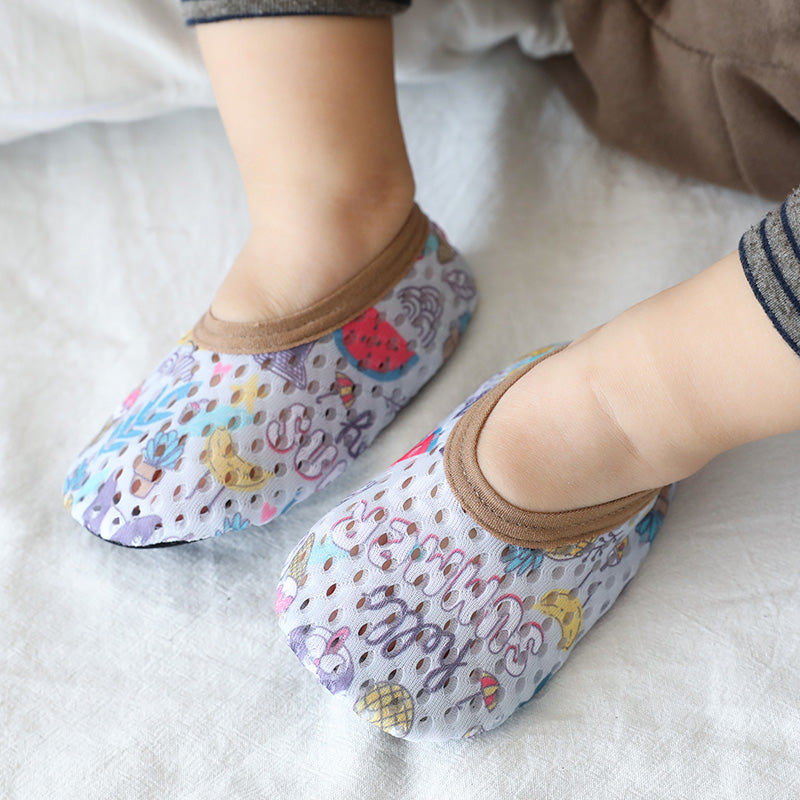 Close-up of a child's feet wearing colorful, patterned socks with brown cuffs. The design features various playful illustrations, including animals and fruits, on a light background.