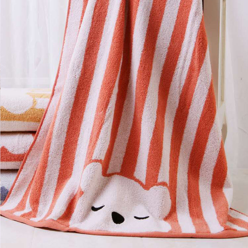 Striped towel with orange and white vertical bands, featuring a cute sleeping bear face at the bottom. Draped over other folded towels in a bright room.