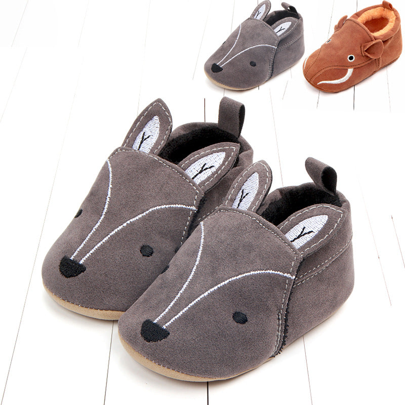 Gray suede baby slippers with embroidered animal faces and ears, resembling a small creature. On the side, a brown slipper with a smiling face is visible.