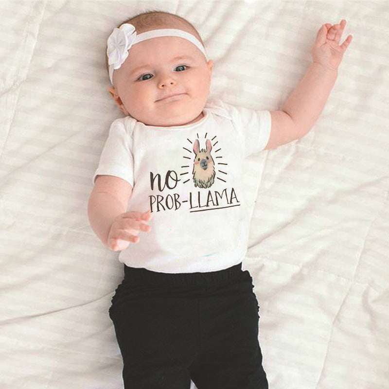 Baby lying on a white blanket, wearing a headband and a white shirt with a llama graphic and the text "No Prob-Llama." The baby has one arm raised and is smiling slightly.