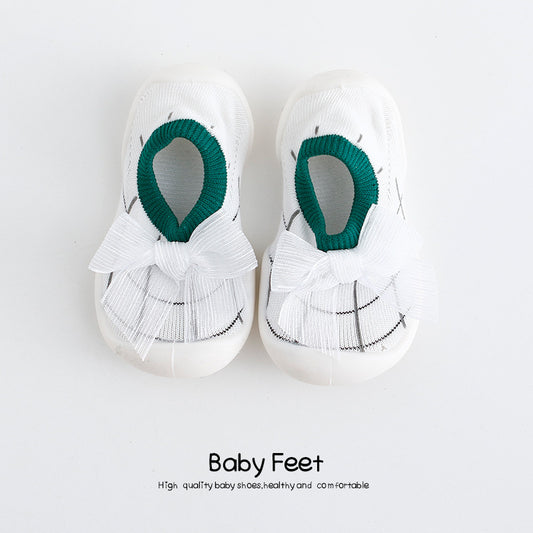 White baby shoes with green trim and white ribbon bows, placed on a plain background. The text below reads "Baby Feet," emphasizing quality, comfort, and health.