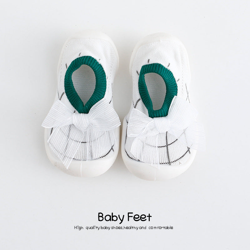 White baby shoes with green trim and white bows, featuring a soft fabric design and rounded toes. Text below reads "Baby Feet" with a description of high quality and comfort.
