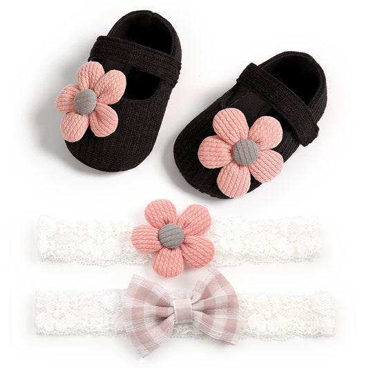 Black baby shoes with pink flower accents and two lace headbands are displayed. One headband features a pink flower, and the other has a pink and white plaid bow.