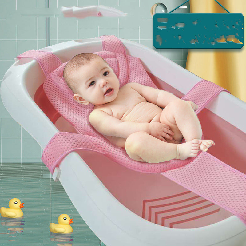 A baby in a pink bath seat inside a white bathtub with two yellow rubber ducks floating in the water. A towel and blurred sign are visible in the tiled bathroom background.