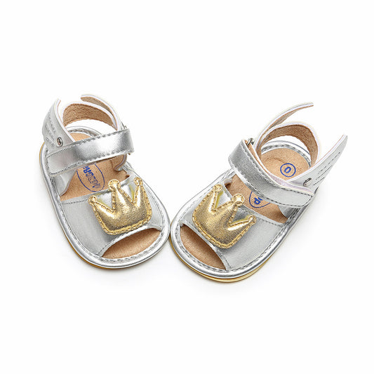 Silver toddler sandals with Velcro straps, featuring gold crown appliqués on the toes, displayed against a white background.
