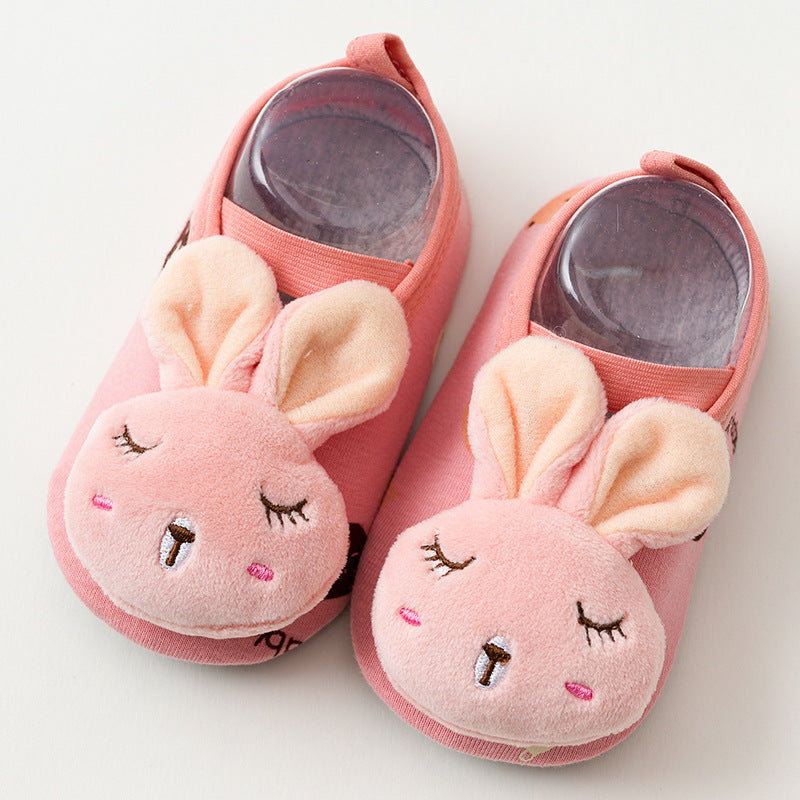 Pink baby slippers featuring plush bunny faces with closed eyes and floppy ears. The soft, cozy design includes light pink and cream accents, perfect for keeping little feet warm.