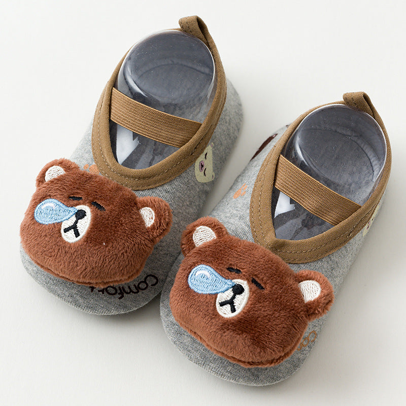 Gray baby shoes with brown bear faces and blue accents on the toes. Brown straps secure the shoes, and paw prints are visible on the fabric. Displayed on a neutral background.