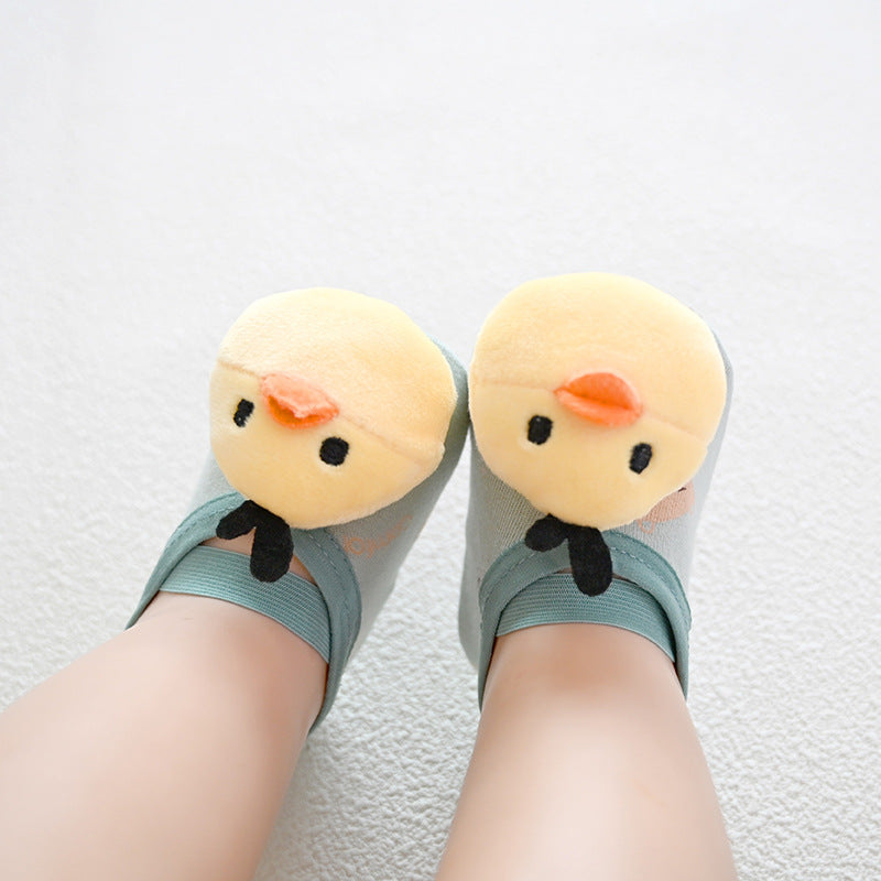 Feet wearing light green socks with plush yellow duck faces on top, placed on a white carpeted floor.