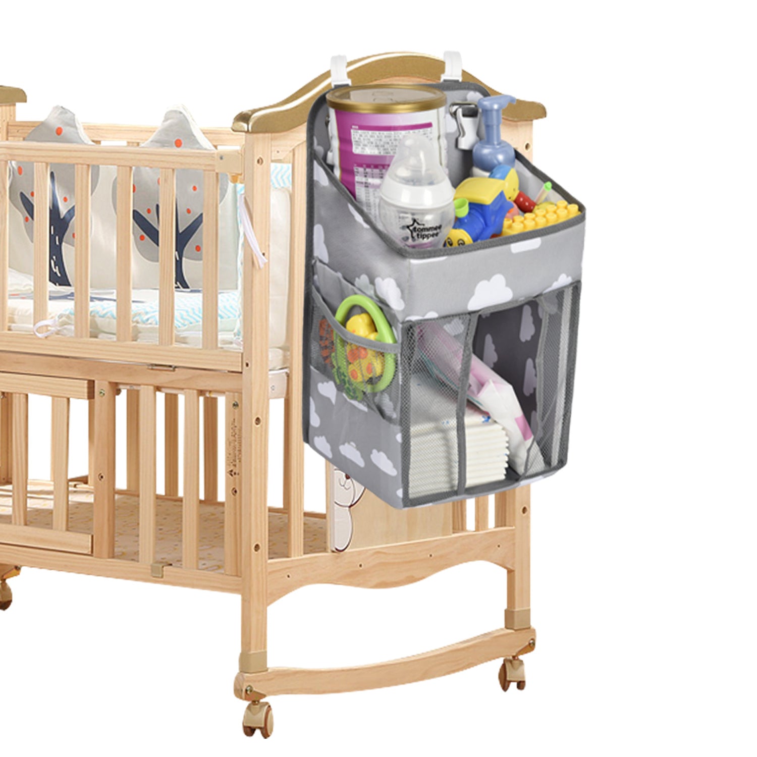 Gray crib organizer with cloud design, attached to a wooden crib. Filled with baby essentials like bottles, toys, wipes, and diapers. Crib has animal-themed bedding.