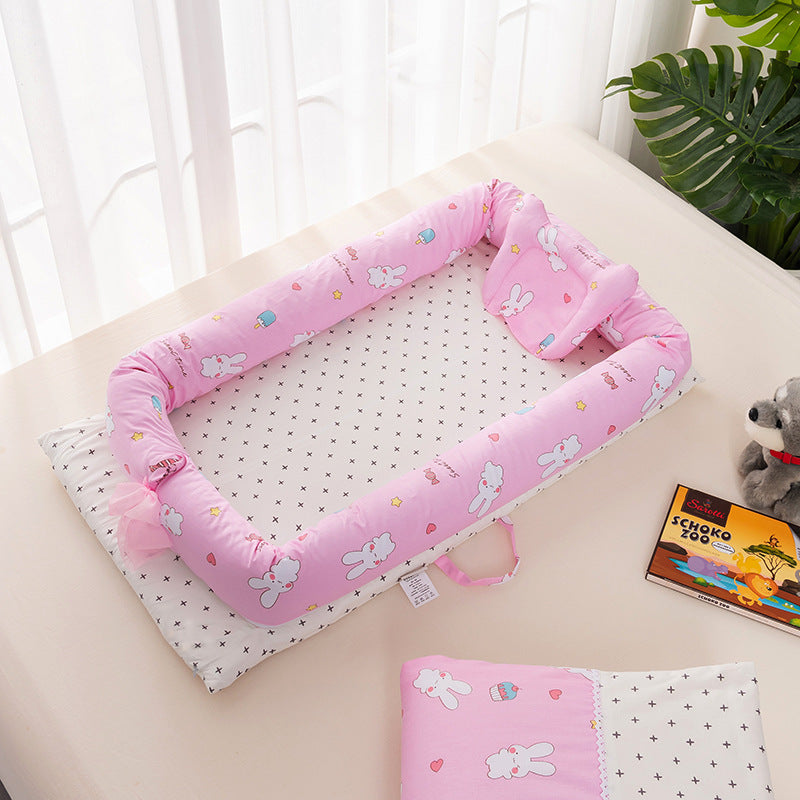 A pink baby crib with a bunny pattern on a white, patterned sheet. There's a small pillow and a book nearby, along with a plush toy in the background.