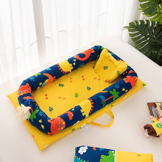 Bright baby nest with a yellow base featuring colorful dinosaur patterns and leafy designs. The set includes a matching yellow pillow and a plush toy nearby on a light surface.