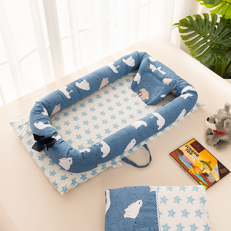 Blue baby nest with polar bear print, featuring a star-patterned base. It is placed on a light surface with a toy dog and a colorful book nearby, next to a potted plant.