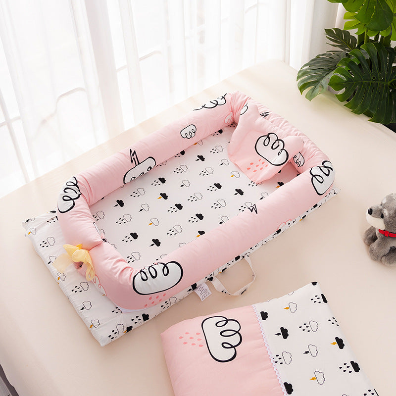 Pink baby playpen with cloud and raindrop patterns, surrounded by soft, cushioned sides. Nearby, a matching blanket and a plush toy bear sit on a light surface.