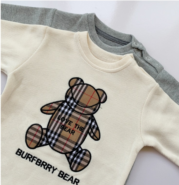 Two folded baby sweaters: a cream one on top with a plaid teddy bear and text "LOVE THE BEAR BURFBRRY BEAR," and a gray one underneath with button details.